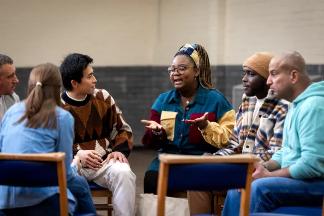 Youth Worker sitting in a group of people and taking. 